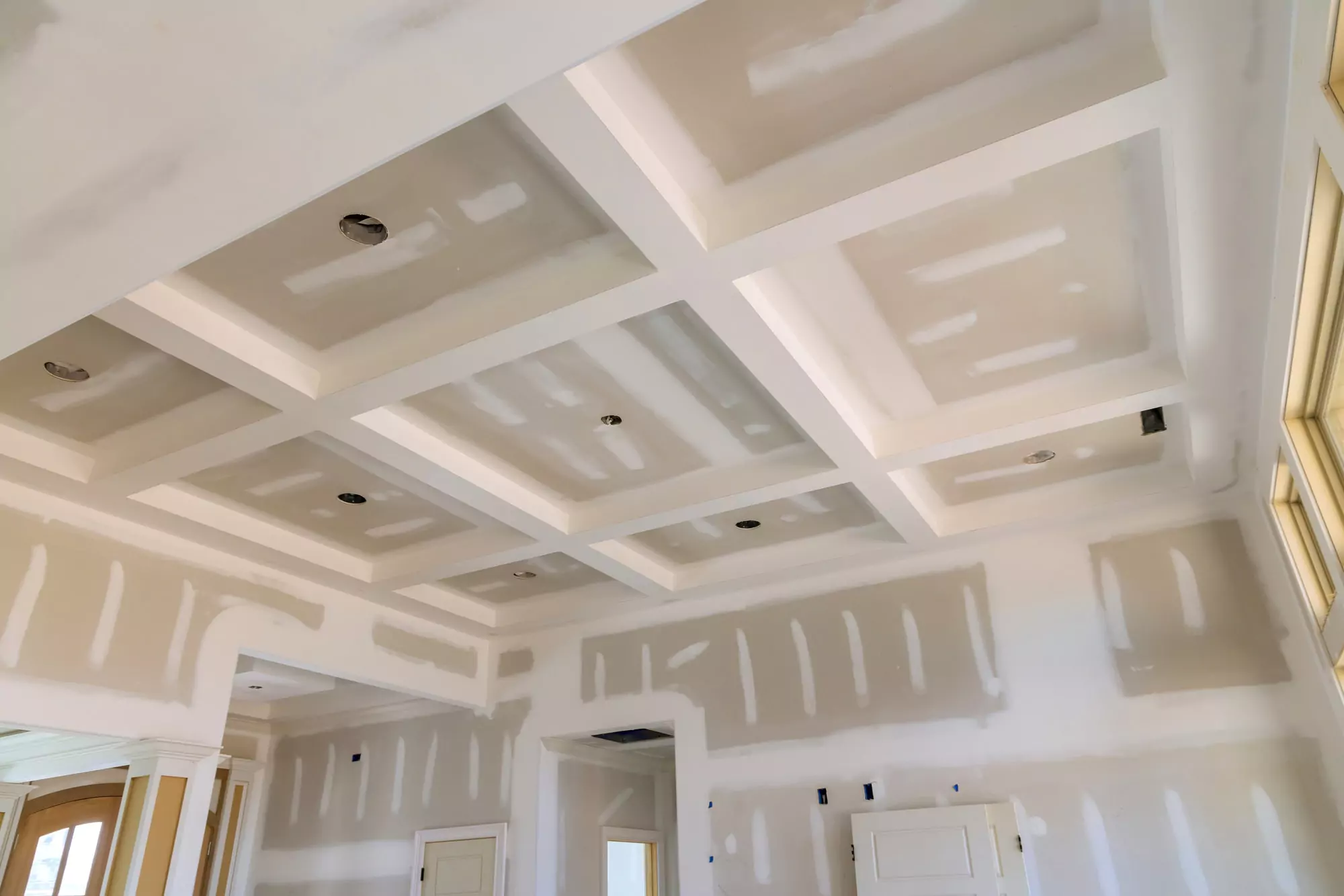 Ein im Bau befindlicher Raum mit der Installation von Trockenbauwänden und abgehängten Deckenplatten sowie Aussparungen für Beleuchtungskörper.