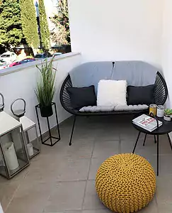 Ein kleiner Außenbalkon mit einer gemütlichen Sitzecke mit einem schwarzen Drahtsofa, grauen und weißen Kissen, einem gelben Strickpouf, einem kleinen schwarzen Tisch mit Dekor und Getränken sowie Topfpflanzen.