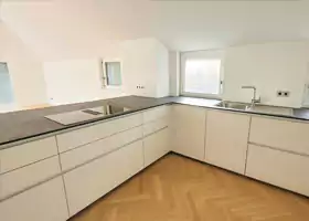 Eine moderne, minimalistische Küche mit weißen Schränken, einem eingebauten Kochfeld, einer Spüle und Hartholzböden.