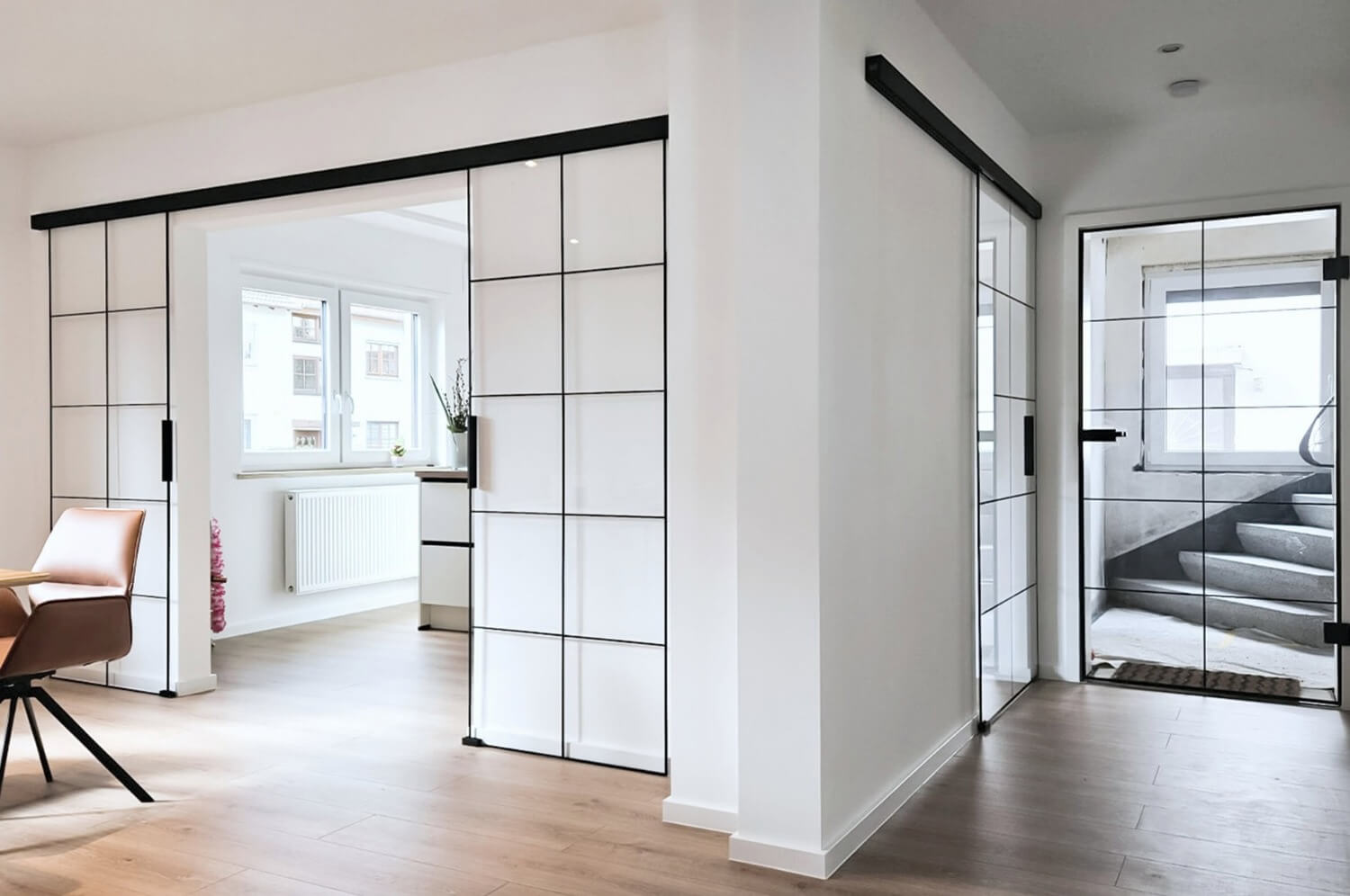 Helles, modernes Interieur eines Einfamilienhauses mit Glasschiebetüren mit schwarzen Rahmen, beigem Boden, einem hölzernen Esstisch mit Stühlen, weißen Wänden und reichlich natürlichem Licht durch große Fenster – das Ergebnis einer energetischen Renovierung.