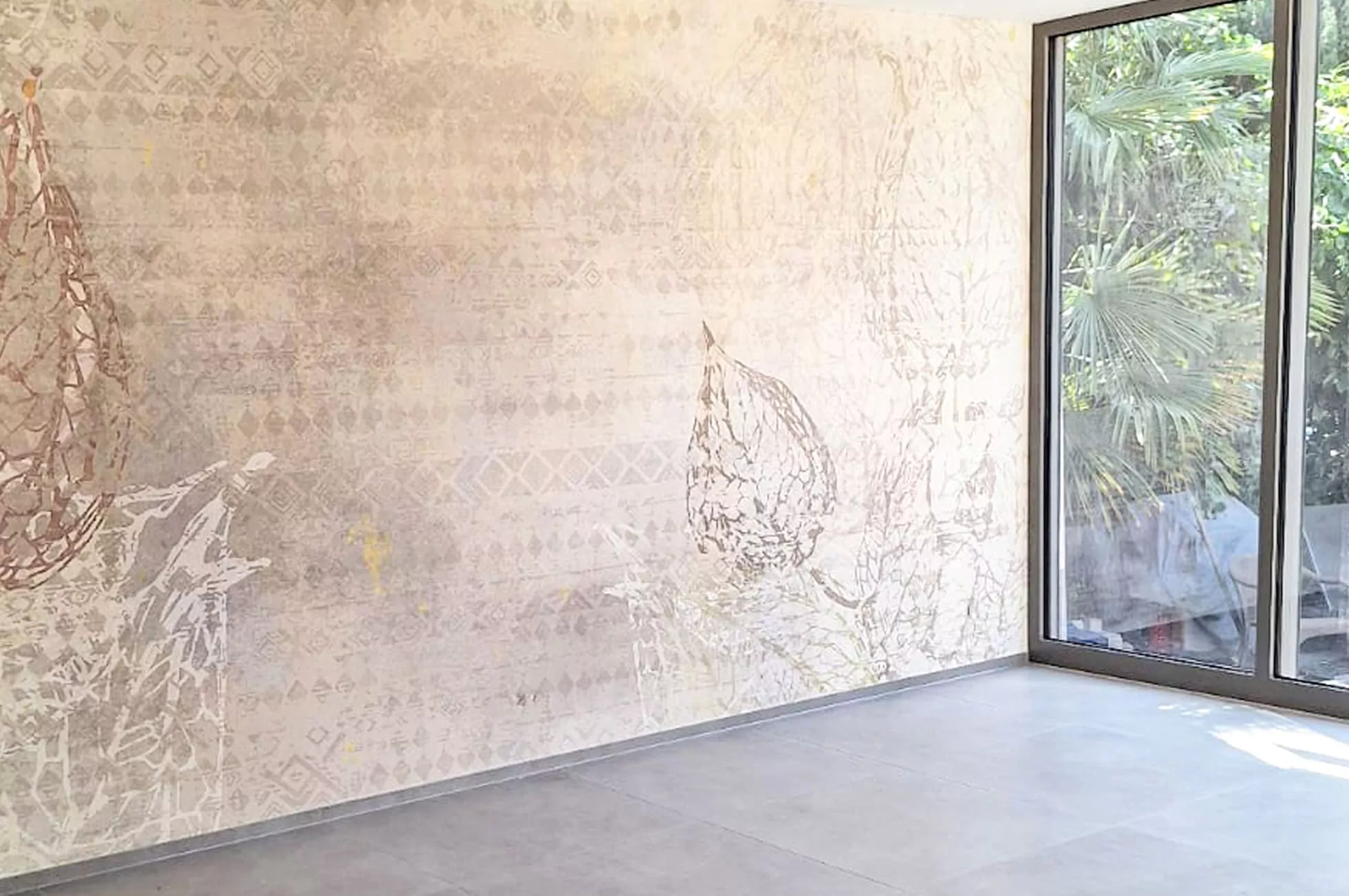 Ein modernes Interieur mit einer dezent gemusterten Wand, großen Fenstern vom Boden bis zur Decke und Blick auf üppiges Grün draußen. Der Raum, der seine jüngste Hausrenovierung zeigt, hat mit seinem grauen Bodenbelag eine minimalistische, geräumige Atmosphäre.