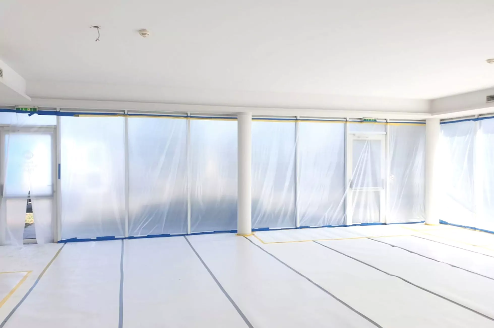 Ein Raum wird umgebaut, die Wände und der Boden sind mit Plastikfolien bedeckt und die Abdeckungen sind mit blauem Malerband befestigt.
