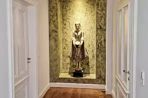 Ein Flur mit Holzboden in einer Heidelberger Villa führt zu einer Nische, in der eine stehende Statue eine Schale hält, die vor einem eleganten Anstrich in grüner Marmoroptik steht.